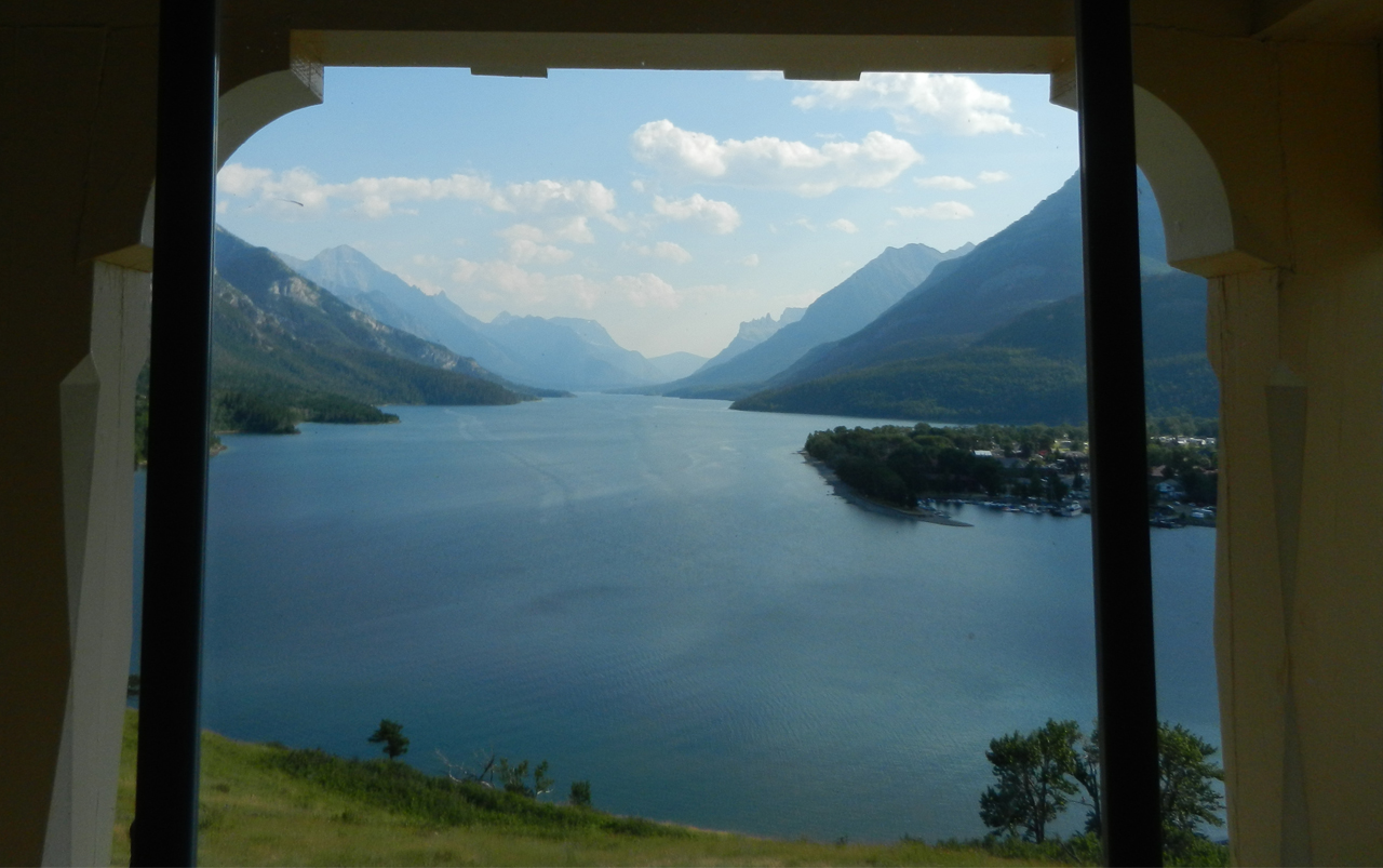 Photo looking through a window to a lake with mountains in the background