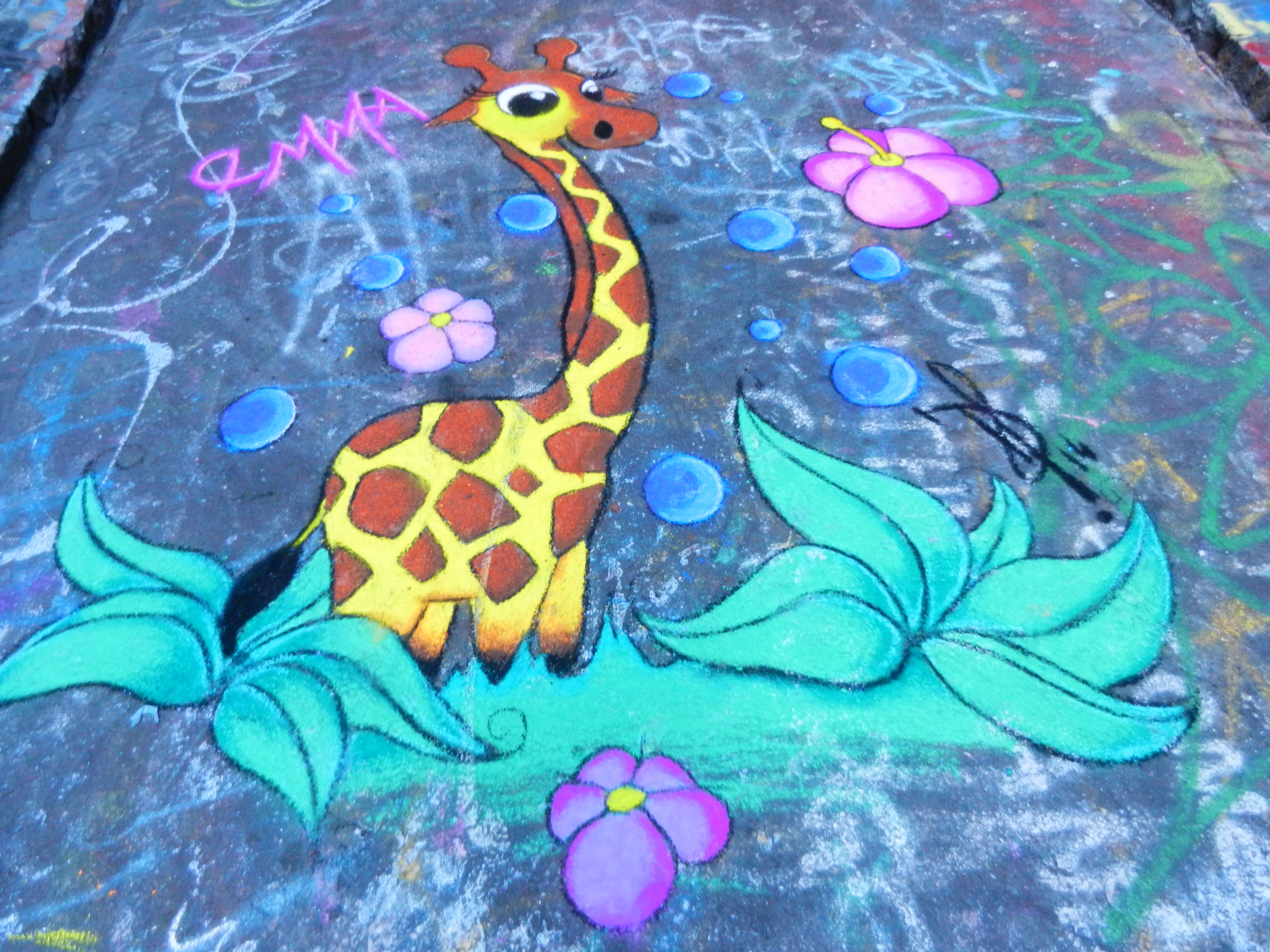 Brightly colored giraffe with flowers and greenery painted on a street.