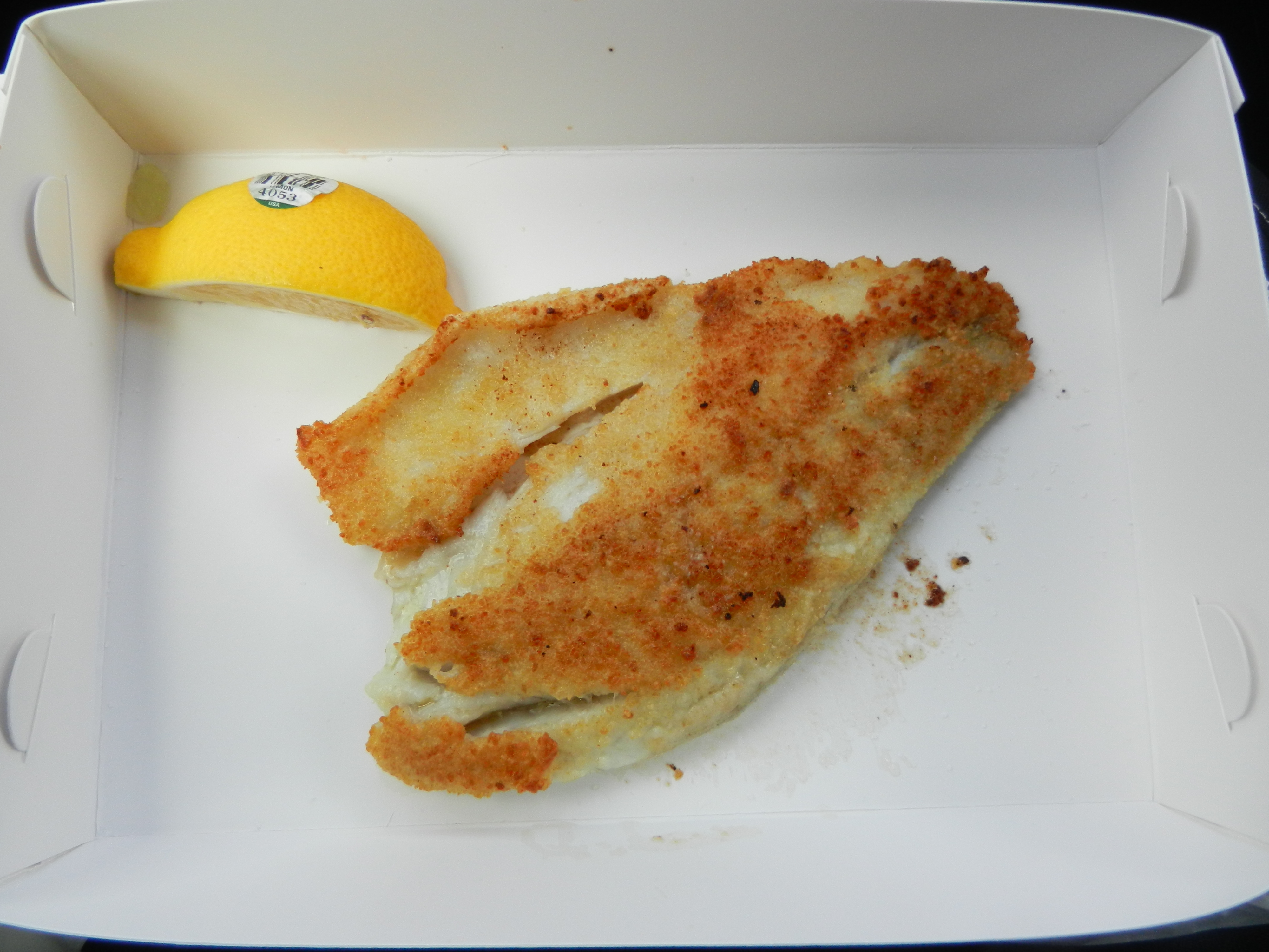Breaded fish with a lemon wedge inside a white cardboard dish.