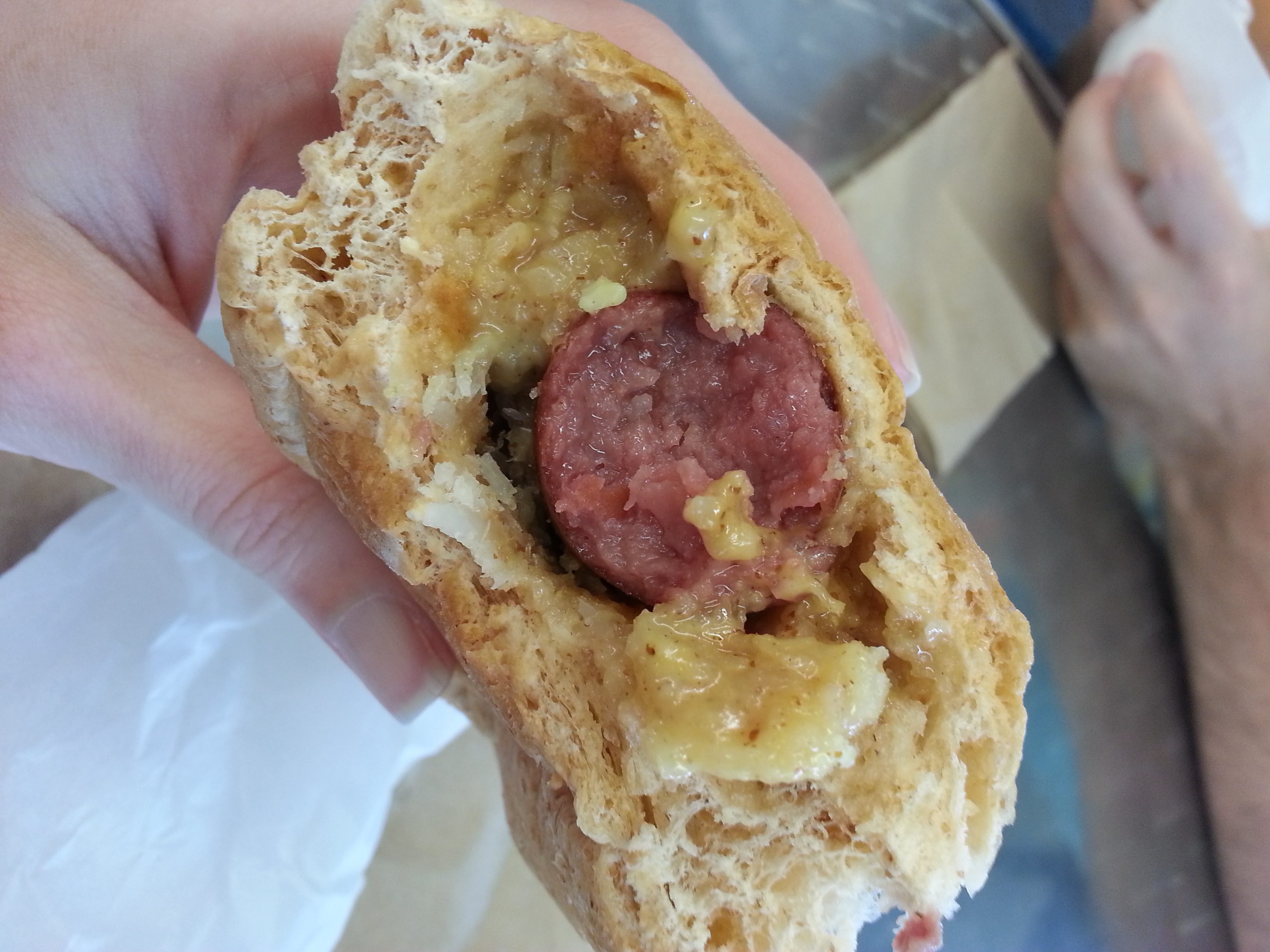 Hand holding a hot dog encased in a roll.