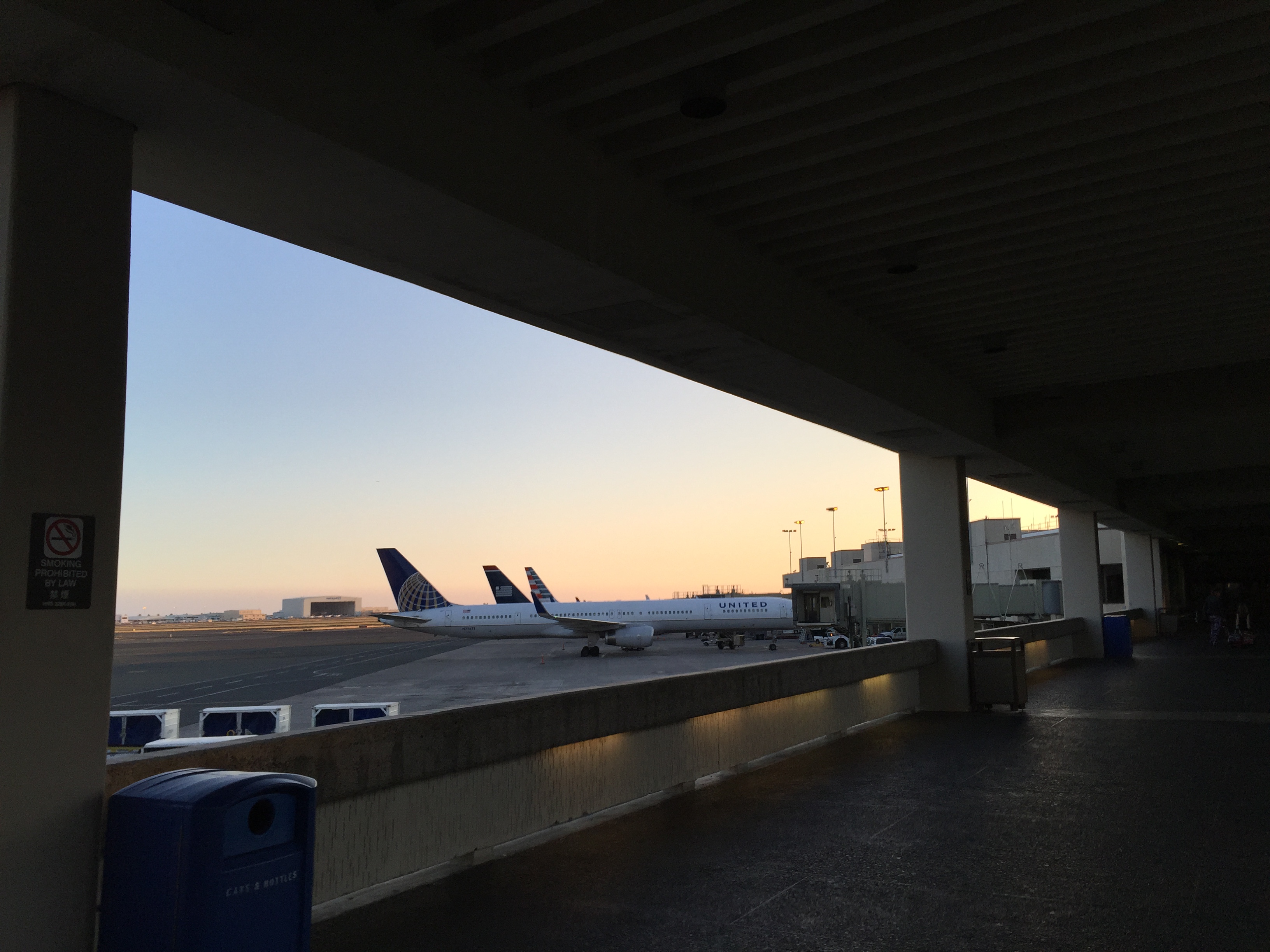 Airplanes parked at airport gates viewed through an opening in an airport walkway.