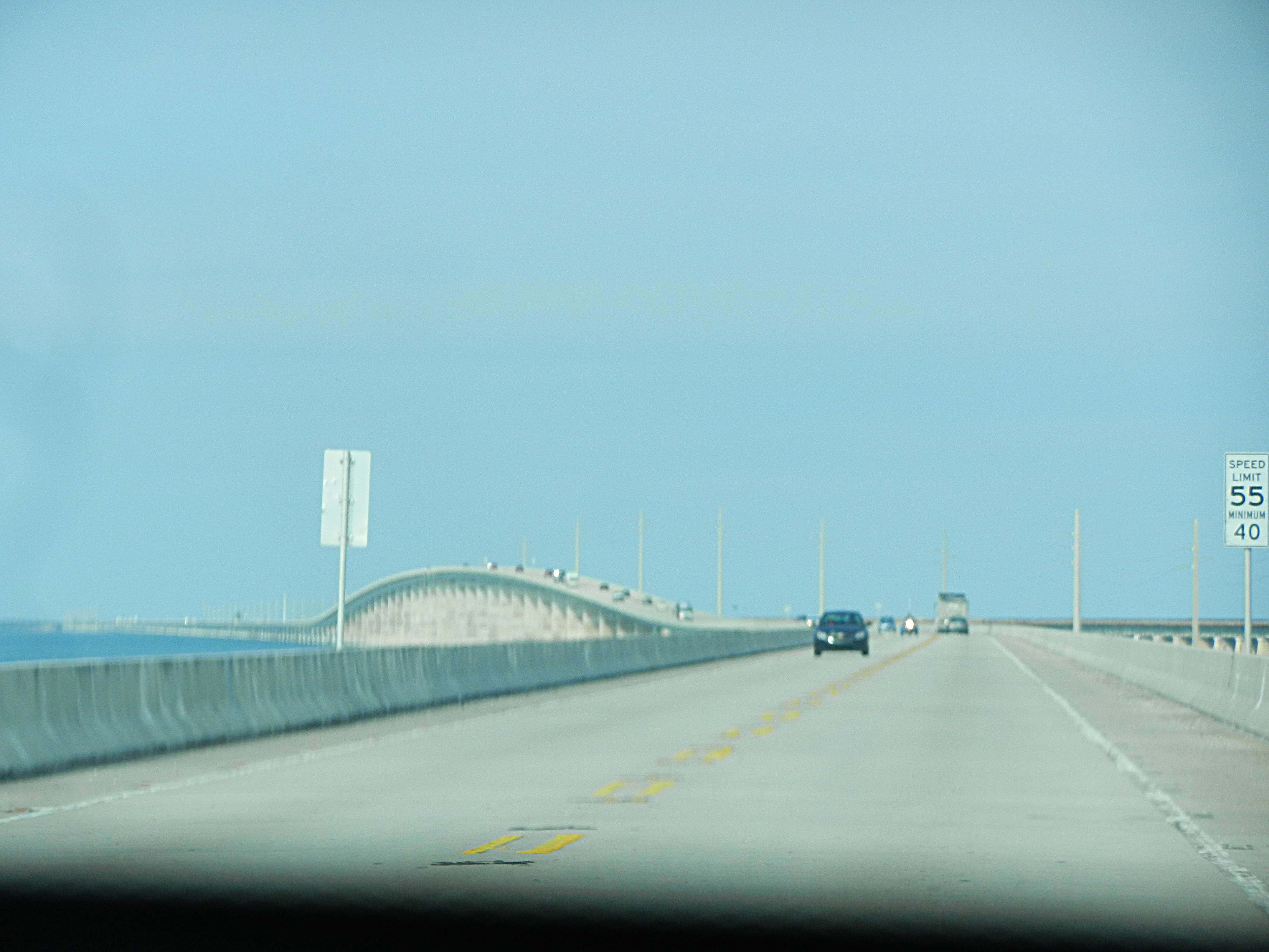 Photo looking out through the windshield of a car at a bridge that is 7 miles long and curves around to the left.