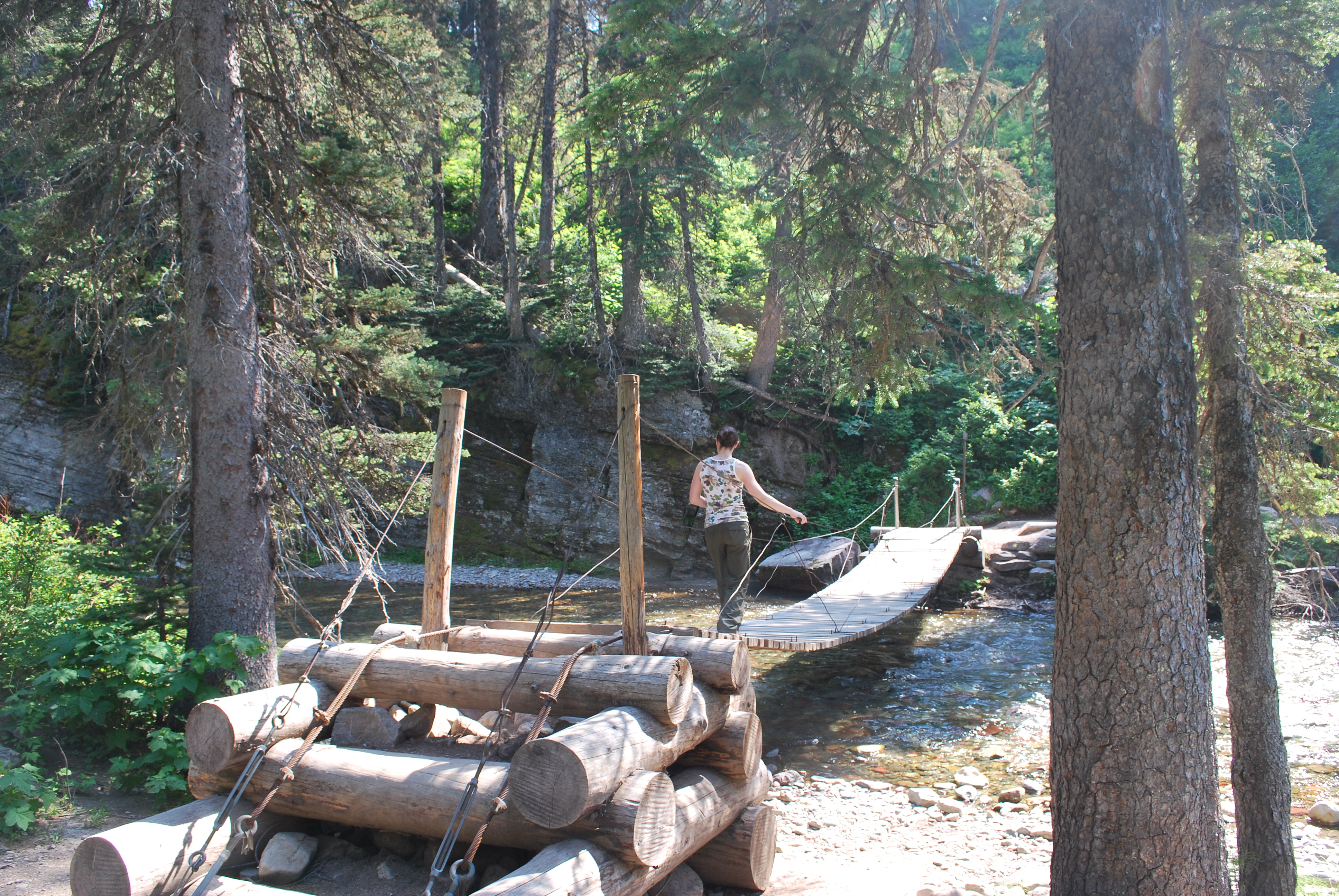 Adult female crossing a small wooden suspension bridge surrounded by forest.
