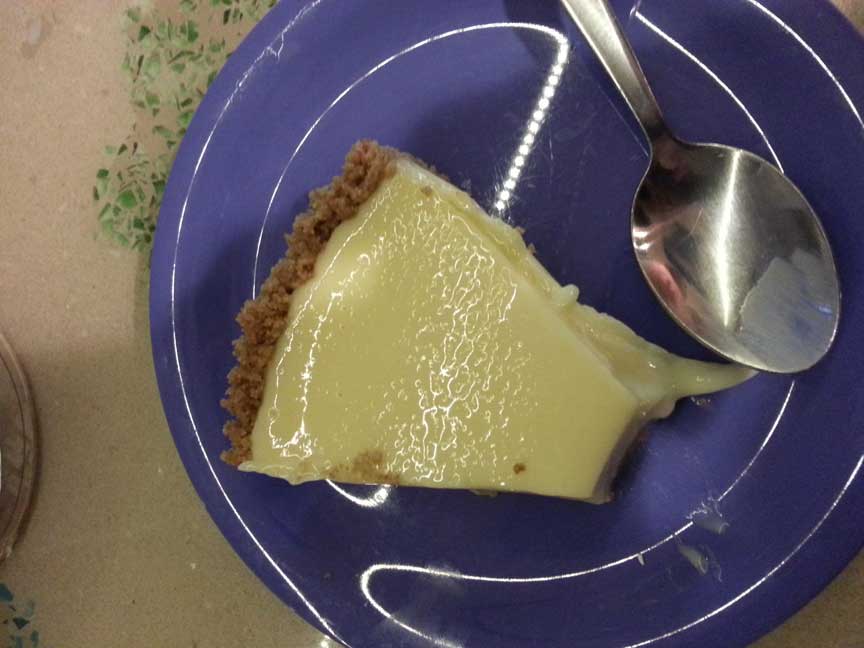 Slice of key lime pie on a dark blue plate sitting on a light brown counter.