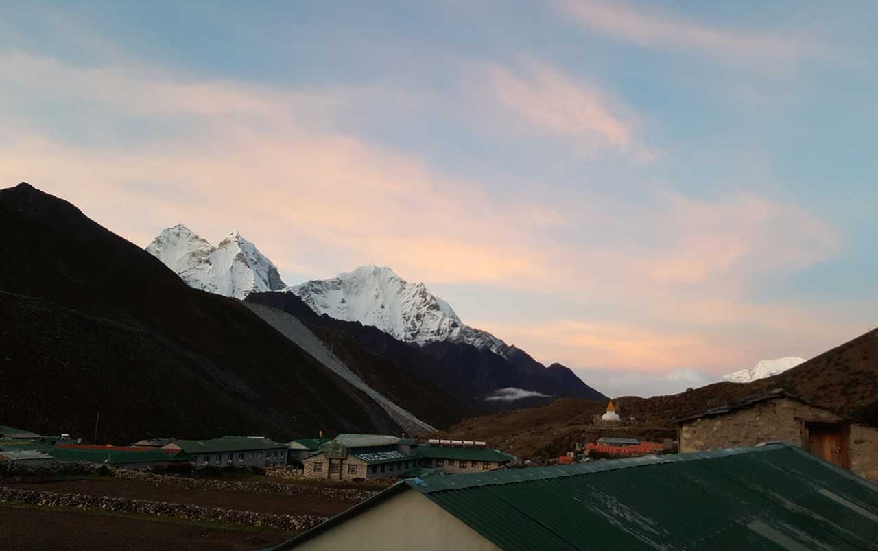 Snow capped mountain peaks surrounding a village in the valley against a blue sky with pink clouds at sunrise.