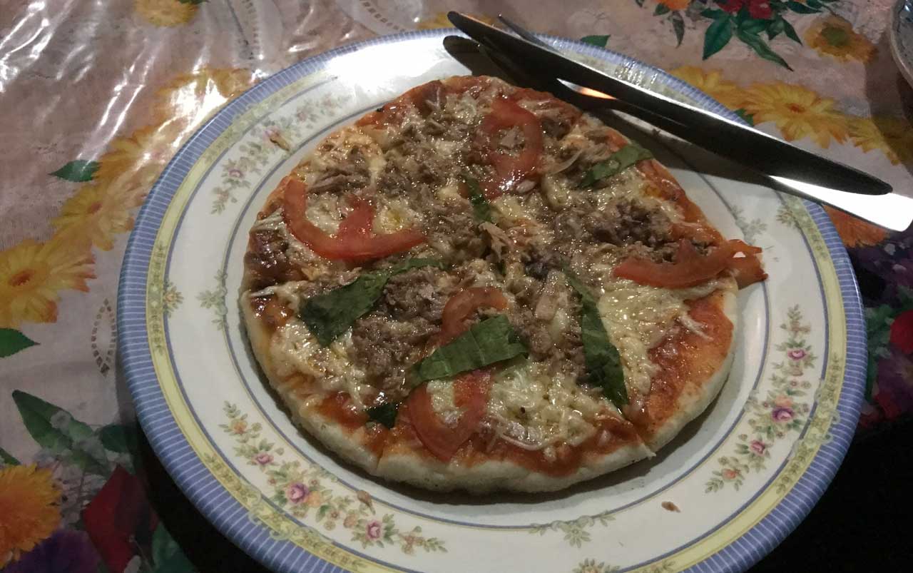 Floral printed plate with a small pizza topped with tuna, cheese, tomatoes, and basil.